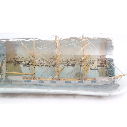 1129 - A 20thC scratch built ship in bottle with postcard backdrop depicting a waterfront with boats and bu... 