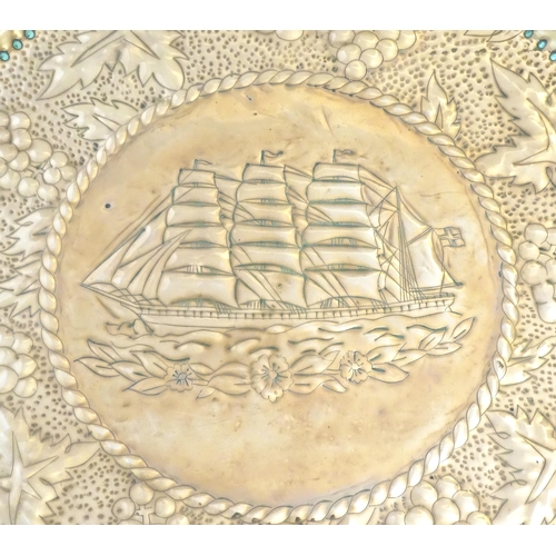 1271 - A large Arts & Crafts copper charger with embossed decoration depicting a ship at sea bordered by fr... 