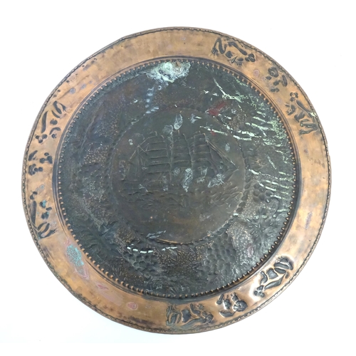 1271 - A large Arts & Crafts copper charger with embossed decoration depicting a ship at sea bordered by fr... 