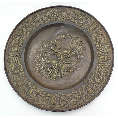 1272 - A large 20thC Continental embossed brass charger decorated with a bucolic central scene with figures... 