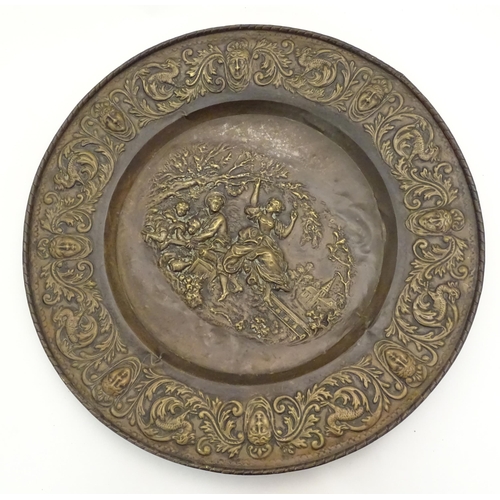 1272 - A large 20thC Continental embossed brass charger decorated with a bucolic central scene with figures... 