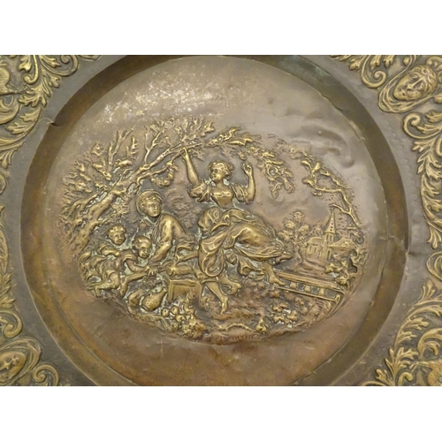 1272 - A large 20thC Continental embossed brass charger decorated with a bucolic central scene with figures... 