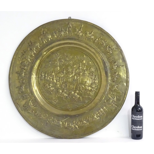 1273 - A large 20thC Indian brass charger with embossed decoration depicting an Indian procession with Impe... 