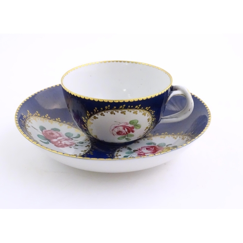 74 - A Continental cup and saucer the blue ground decorated with hand painted panels depicting floral ros... 