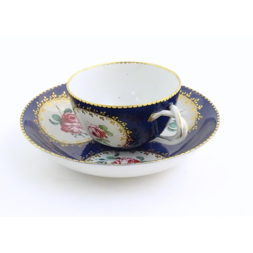 74 - A Continental cup and saucer the blue ground decorated with hand painted panels depicting floral ros... 