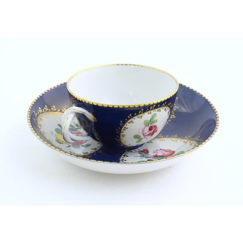 74 - A Continental cup and saucer the blue ground decorated with hand painted panels depicting floral ros... 