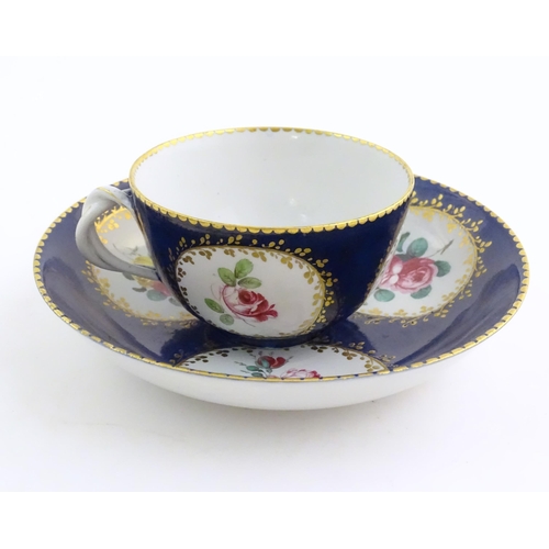 74 - A Continental cup and saucer the blue ground decorated with hand painted panels depicting floral ros... 