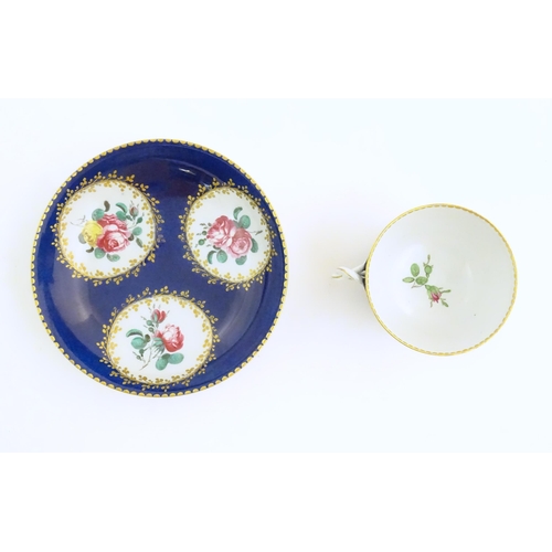 74 - A Continental cup and saucer the blue ground decorated with hand painted panels depicting floral ros... 