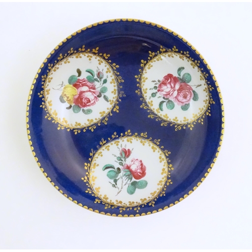 74 - A Continental cup and saucer the blue ground decorated with hand painted panels depicting floral ros... 