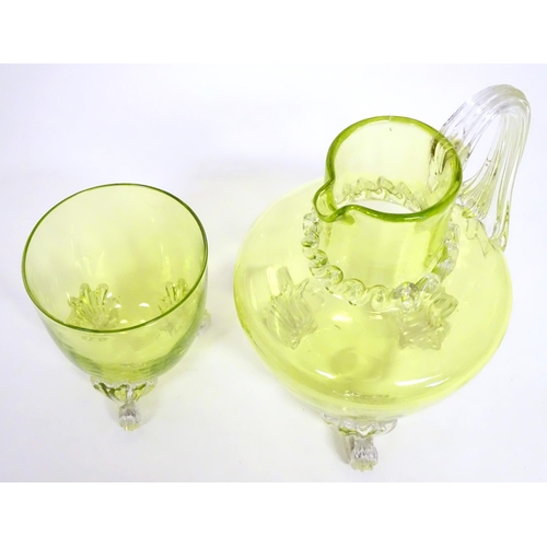 268 - A yellow glass water jug with clear glass handle and feet, together with a matching glass. The jug  ... 