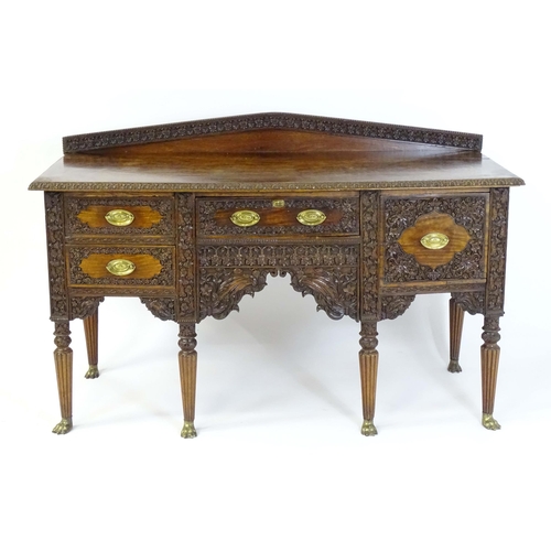 A late 19thC Anglo-Indian sideboard with a profusely detailed carved carcass and drawer fronts, a shaped carved upstands and raised on Gillows style reeded tapering legs terminating in brass lions paw feet. 63" wide x 27" deep x 40" high.