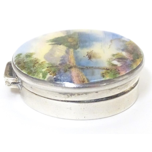 356 - A silver pill box, the hinged lid decorated with a guilloche enamel landscape scene depicting figure... 