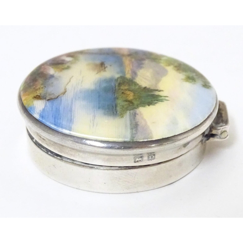 356 - A silver pill box, the hinged lid decorated with a guilloche enamel landscape scene depicting figure... 