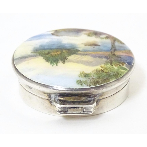 356 - A silver pill box, the hinged lid decorated with a guilloche enamel landscape scene depicting figure... 