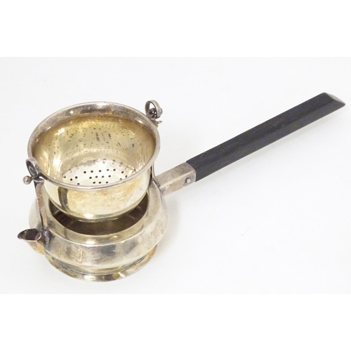 396 - A silver tea strainer modelled as a stylised teapot with suspended strainer above, the base with pou... 