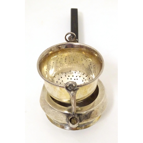 396 - A silver tea strainer modelled as a stylised teapot with suspended strainer above, the base with pou... 