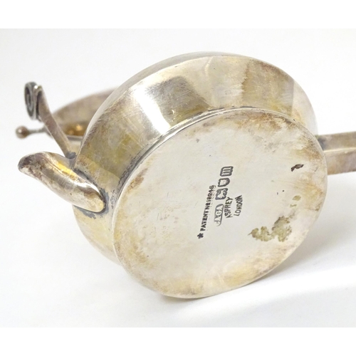 396 - A silver tea strainer modelled as a stylised teapot with suspended strainer above, the base with pou... 