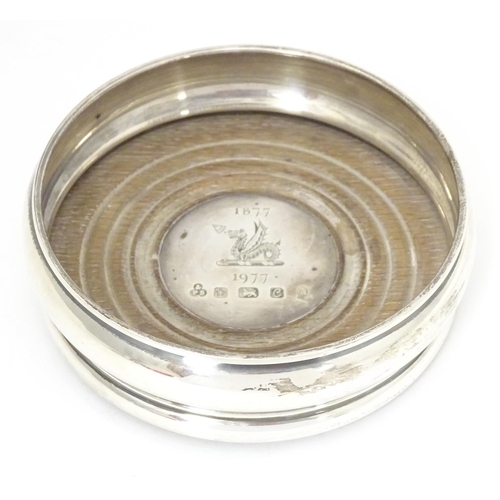 504A - A silver bottle coaster with turned wooden base, hallmarked Sheffield 1977 with silver Jubilee mark,... 