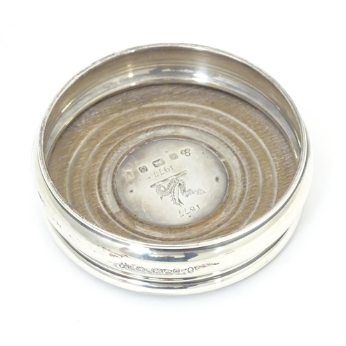 504A - A silver bottle coaster with turned wooden base, hallmarked Sheffield 1977 with silver Jubilee mark,... 