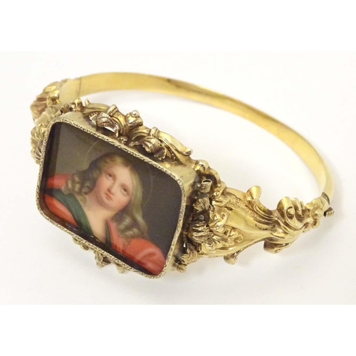 634 - A 19thC gold bangle formed bracelet set with central hand painted ceramic cabochon depicting religio... 