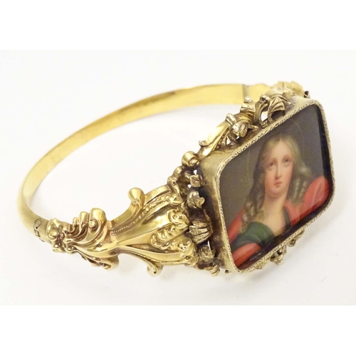 634 - A 19thC gold bangle formed bracelet set with central hand painted ceramic cabochon depicting religio... 