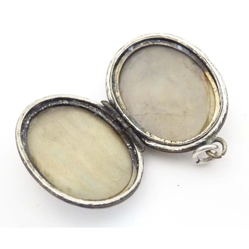 638 - A white metal pendant locket of oval form with foliate decoration 1 1/4