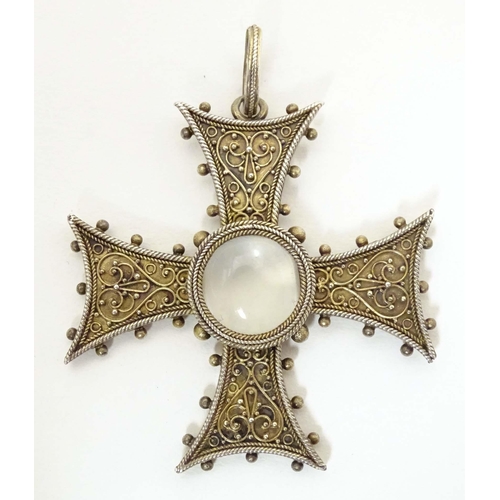 673 - A white metal pendant of cross form with scroll detail, set with central moonstone cabochon. Approx.... 