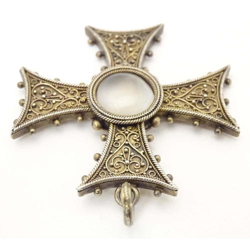 673 - A white metal pendant of cross form with scroll detail, set with central moonstone cabochon. Approx.... 