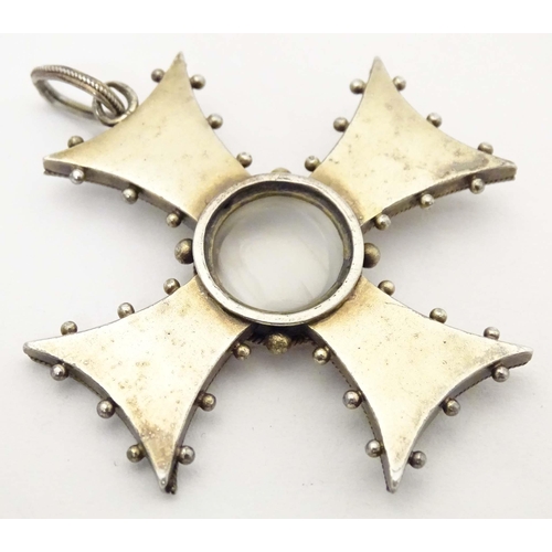 673 - A white metal pendant of cross form with scroll detail, set with central moonstone cabochon. Approx.... 