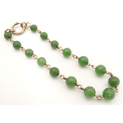 700 - A bracelet of green jade beads with yellow metal links and clasp. Approx. 7 1/2