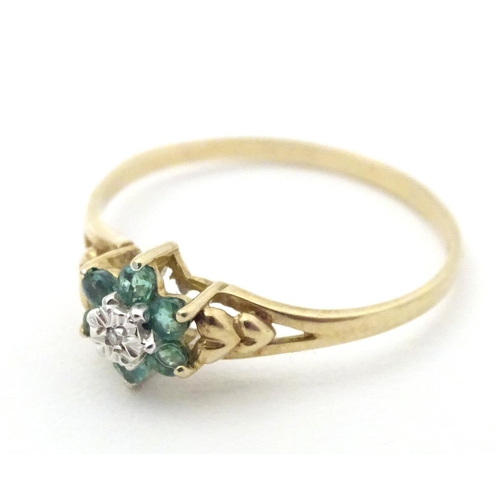 571 - A 9ct gold ring set with central diamond bordered by emeralds. Ring size approx. S 1/2