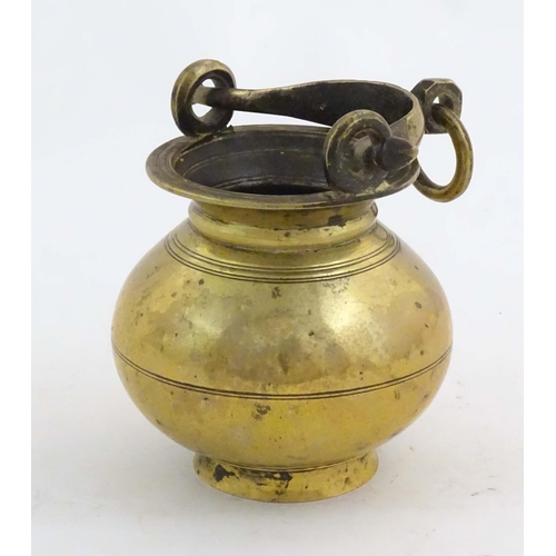 1023 - A brass water pot with bulbous body and swing handle with hanging loop and incised banded decoration... 