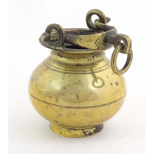 1023 - A brass water pot with bulbous body and swing handle with hanging loop and incised banded decoration... 