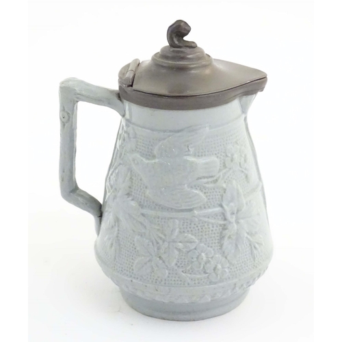 1098 - A Victorian stoneware jug with a pewter lid, the body with moulded decoration depicting birds, flowe... 