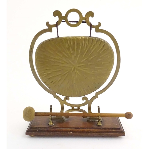 1104 - A 20thC brass table gong within a scrolling brass surround, on a rectangular oak base with beater. R... 