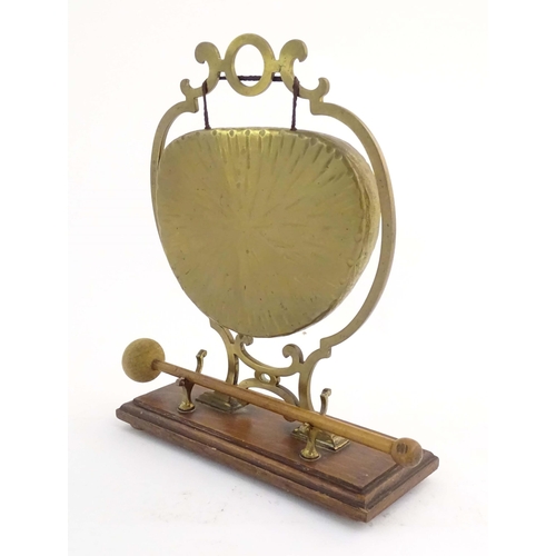 1104 - A 20thC brass table gong within a scrolling brass surround, on a rectangular oak base with beater. R... 