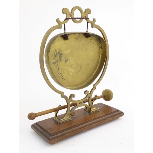 1104 - A 20thC brass table gong within a scrolling brass surround, on a rectangular oak base with beater. R... 