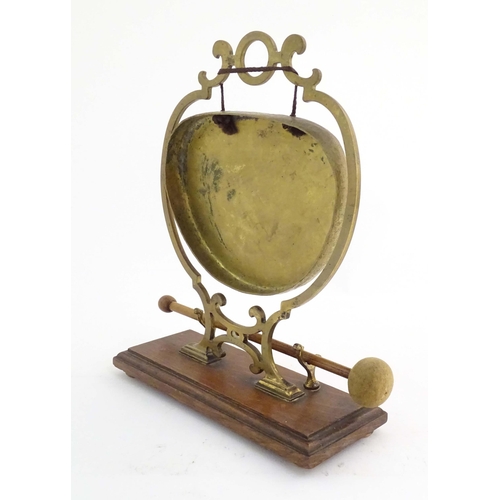 1104 - A 20thC brass table gong within a scrolling brass surround, on a rectangular oak base with beater. R... 