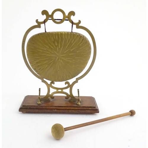 1104 - A 20thC brass table gong within a scrolling brass surround, on a rectangular oak base with beater. R... 