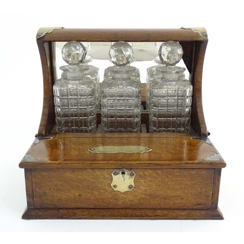 1112 - A late 19th / early 20thC oak tantalus with a mirrored back and silver plate mounts, with three glas... 