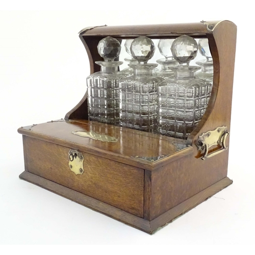 1112 - A late 19th / early 20thC oak tantalus with a mirrored back and silver plate mounts, with three glas... 