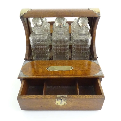 1112 - A late 19th / early 20thC oak tantalus with a mirrored back and silver plate mounts, with three glas... 