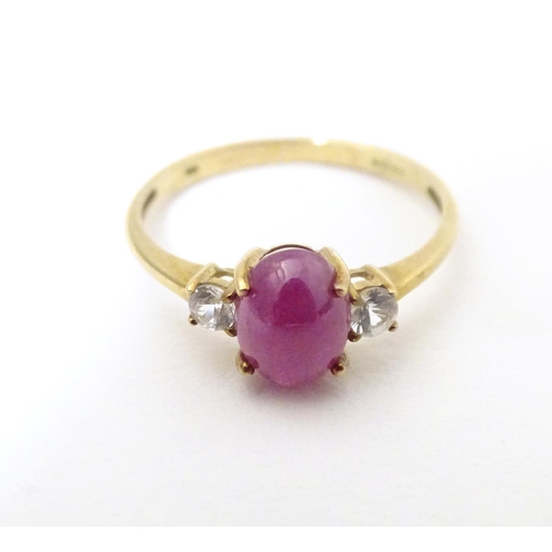 578 - A 9ct gold ring with ruby coloured cabochon flanked by two white stones. Ring size approx. N 1/2