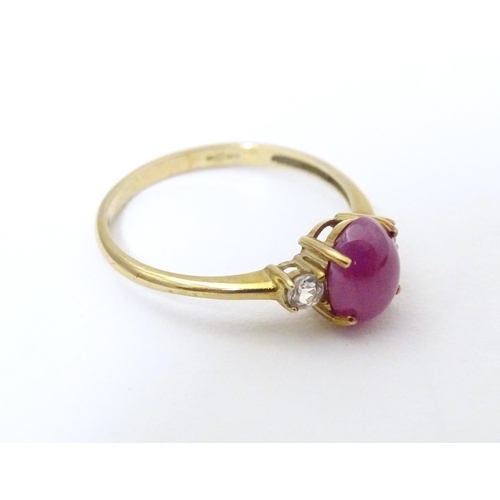 578 - A 9ct gold ring with ruby coloured cabochon flanked by two white stones. Ring size approx. N 1/2