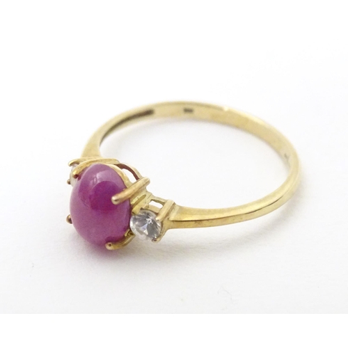 578 - A 9ct gold ring with ruby coloured cabochon flanked by two white stones. Ring size approx. N 1/2