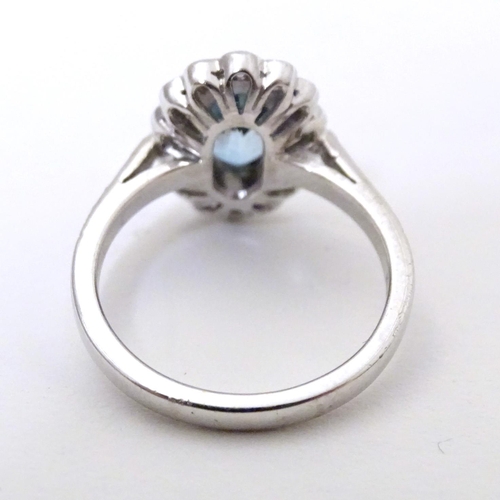 579 - A 9ct white gold ring set with aquamarine coloured oval stone to centre bordered by diamonds with fu... 