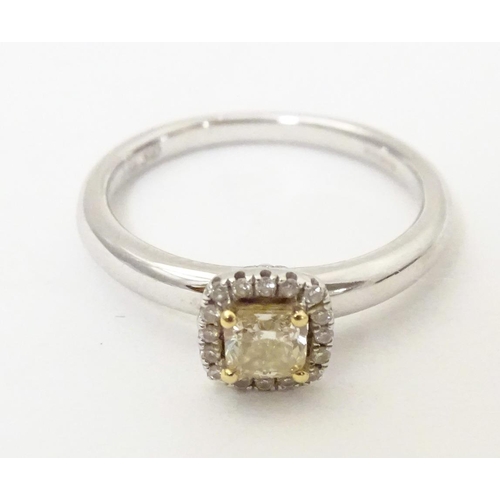 581 - An 18ct white gold ring set with central canary diamond bordered by white diamonds. Ring size approx... 