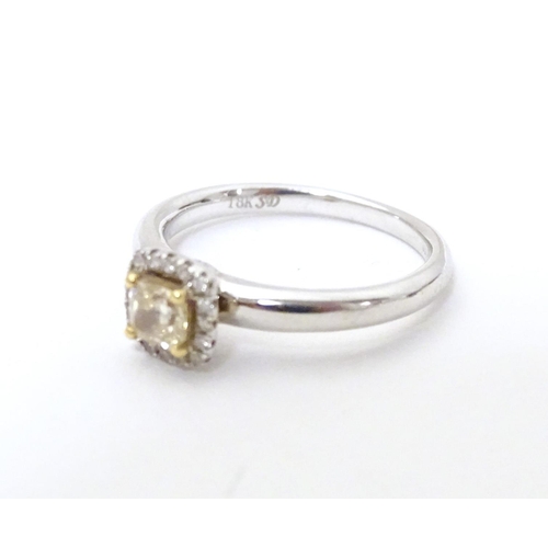 581 - An 18ct white gold ring set with central canary diamond bordered by white diamonds. Ring size approx... 