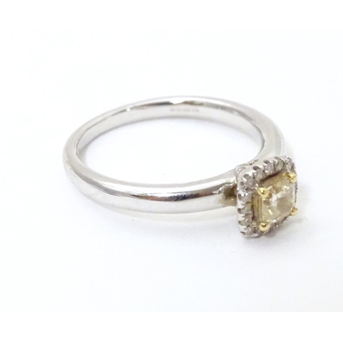 581 - An 18ct white gold ring set with central canary diamond bordered by white diamonds. Ring size approx... 