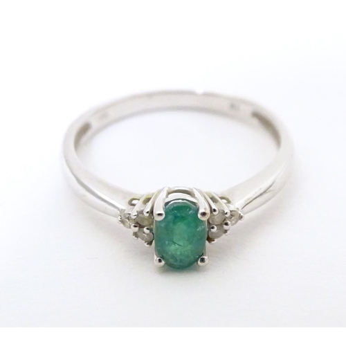 592 - A 10ct white gold ring set with central emerald flanked by three diamonds each shoulder. Ring size a... 